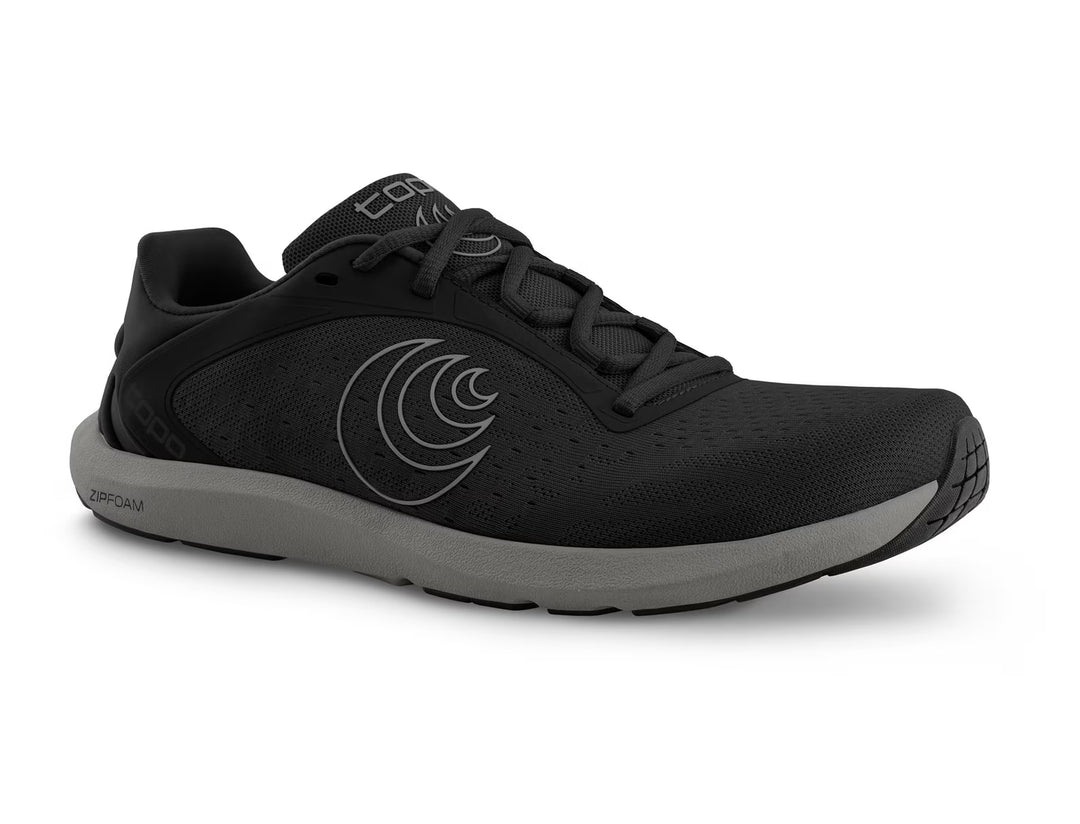 The TOPO ST-6 (Men's) is a black athletic shoe with a gray sole, black laces, and a subtle circular logo. It features a roomy toe box, perforated upper for breathability, and low-profile design inspired by barefoot running.