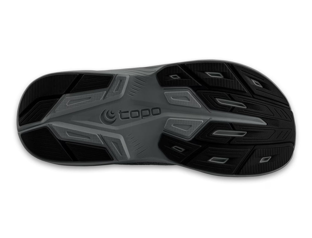 The image shows the black and gray rubber outsole of the TOPO Magnifly 6 (Men's) running shoe, with textured tread patterns and the TOPO brand name in raised letters at the center.