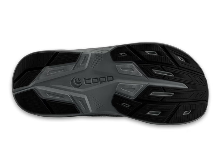 The image shows the black and gray rubber outsole of the TOPO Magnifly 6 (Men's) running shoe, with textured tread patterns and the TOPO brand name in raised letters at the center.