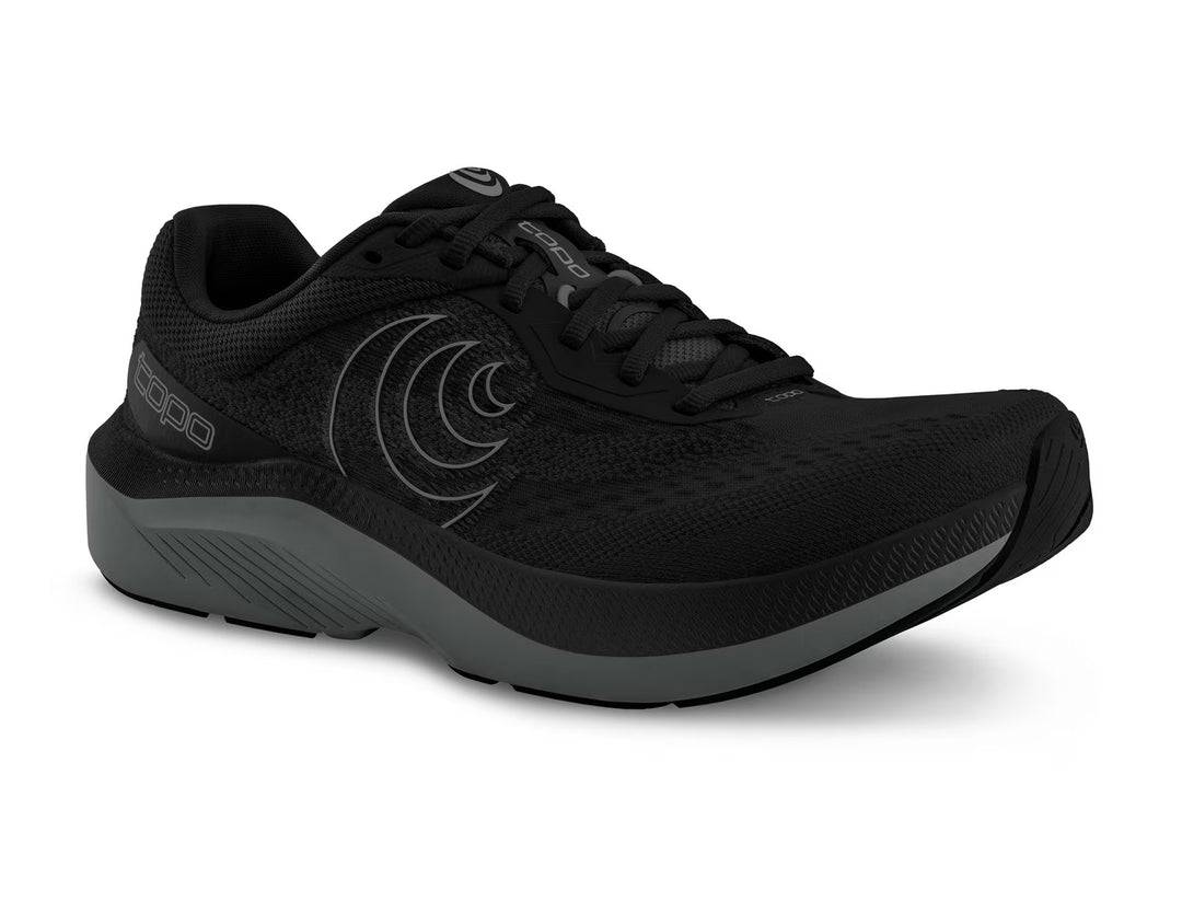 The TOPO Magnifly 6 (Men's) is a black running shoe with a cushioned mesh upper, thick gray ZipFoam midsole, black laces, and subtle wave patterns on the sides.