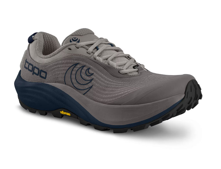 A gray men’s athletic trail running shoe, the TOPO Pursuit 3 features blue accents, a black sole, and TOPO branding on the side. It is equipped with Vibram Megagrip rugged tread for superior traction, traditional laces, and a subtle circular logo near the laces.