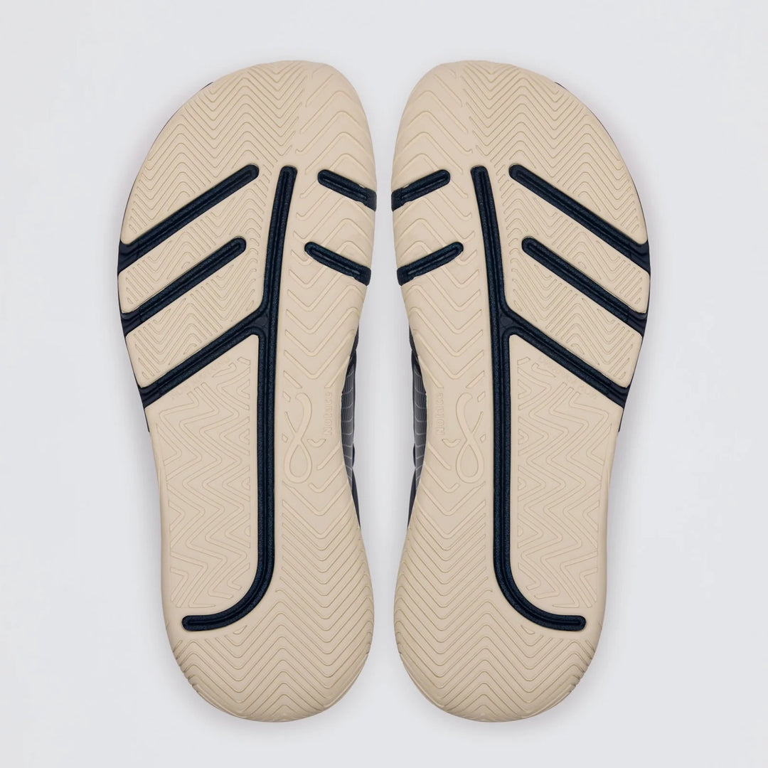 Two beige Koto 1 (Women’s) shoe soles by Notace, featuring black and navy zigzag and curved line patterns, are placed side by side on a white background. They showcase tread designs and textured surfaces for grip, making them ideal for multidirectional control in court or gym shoes.