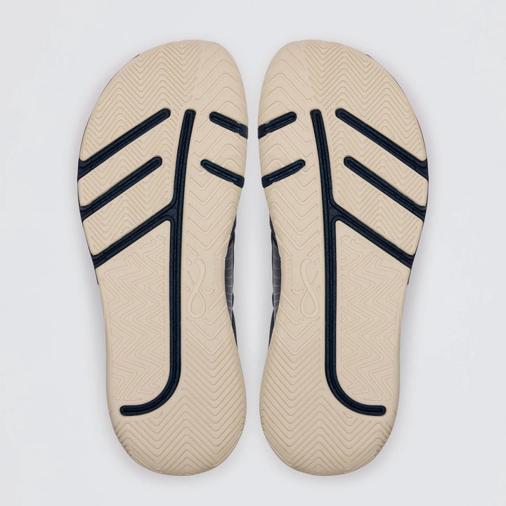 Two beige Koto 1 (Women’s) shoe soles by Notace, featuring black and navy zigzag and curved line patterns, are placed side by side on a white background. They showcase tread designs and textured surfaces for grip, making them ideal for multidirectional control in court or gym shoes.
