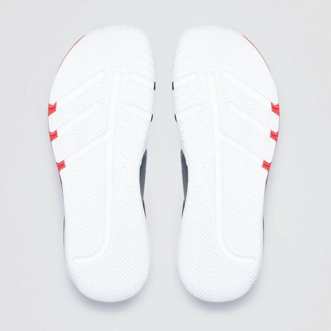 The image shows the white soles of Notace KOTO 1 (Men’s) gym shoes, featuring a textured zigzag tread for multidirectional control and three red stripes on each sole near the heel.