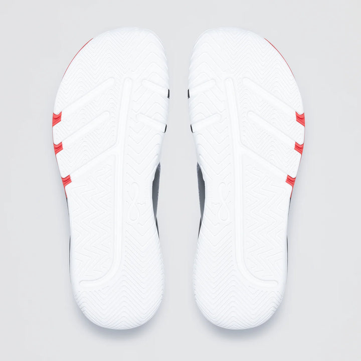 The image shows the white soles of Notace KOTO 1 (Men’s) gym shoes, featuring a textured zigzag tread for multidirectional control and three red stripes on each sole near the heel.
