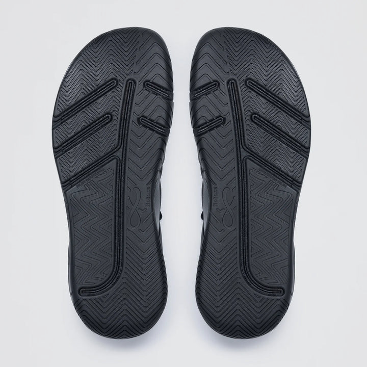 The Notace Koto 1 (Women's) features black court shoe soles with grooved, zigzag, and straight line tread patterns for multidirectional control and stability, displayed side by side on a plain light background.