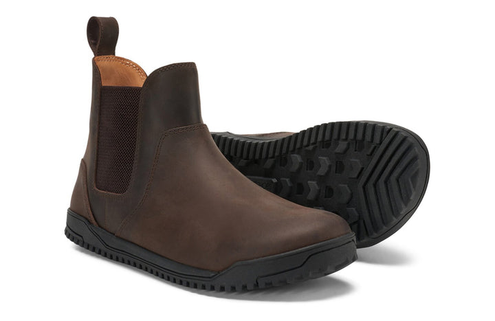 The Ridgeway Chelsea (Men's) are brown slip-on boots with black rubber soles, elastic side panels, and a back pull tab. One boot stands upright; the other lies on its side, showing the tread pattern.