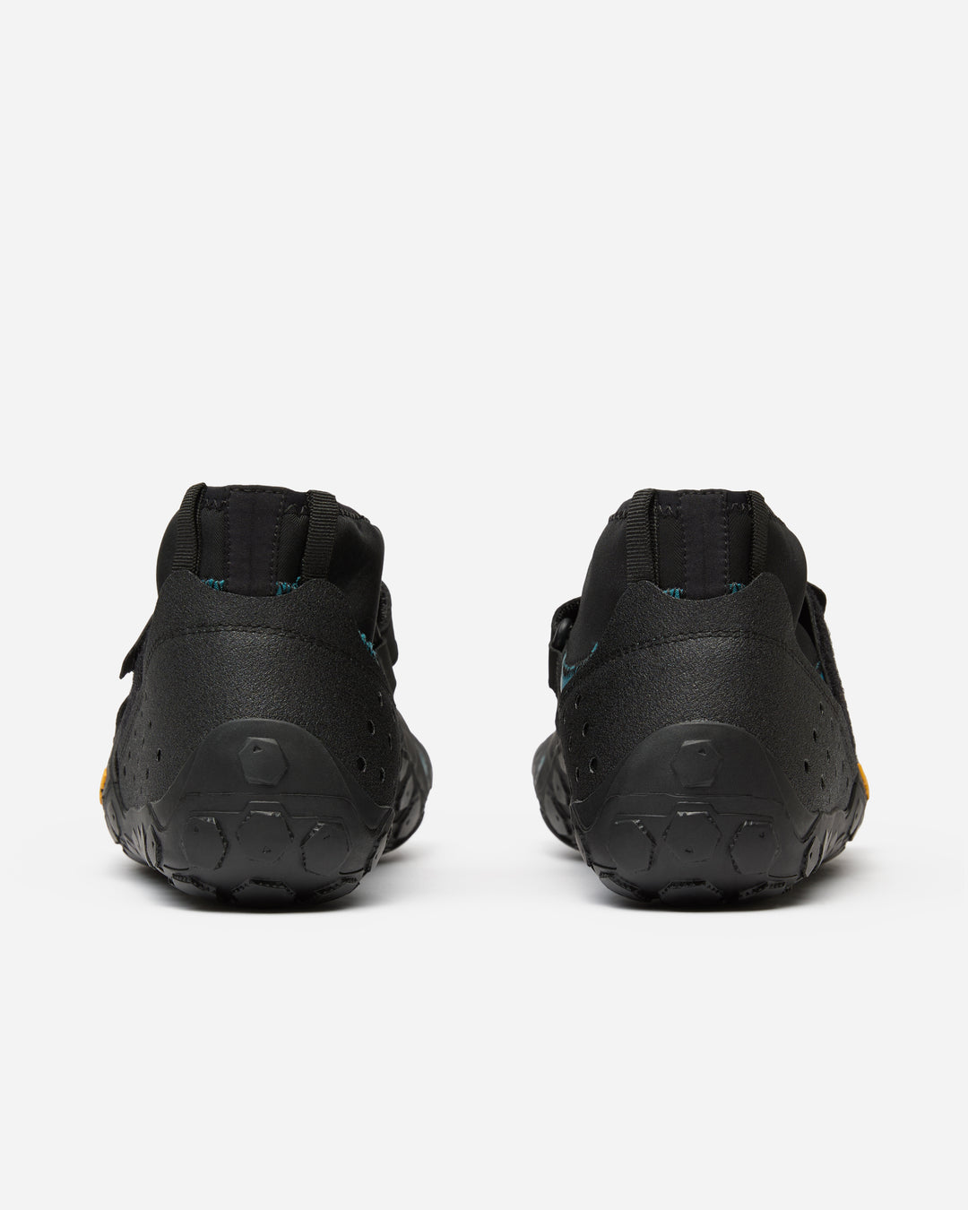 The Vibram Scramkey (Unisex) outdoor shoes are shown from the back on a white background, featuring black minimalist design, low-cut heels, and textured rubber soles with Traction Lug technology.