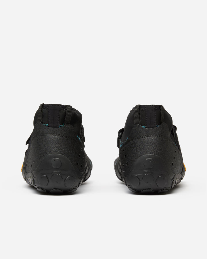 The Vibram Scramkey (Unisex) outdoor shoes are shown from the back on a white background, featuring black minimalist design, low-cut heels, and textured rubber soles with Traction Lug technology.