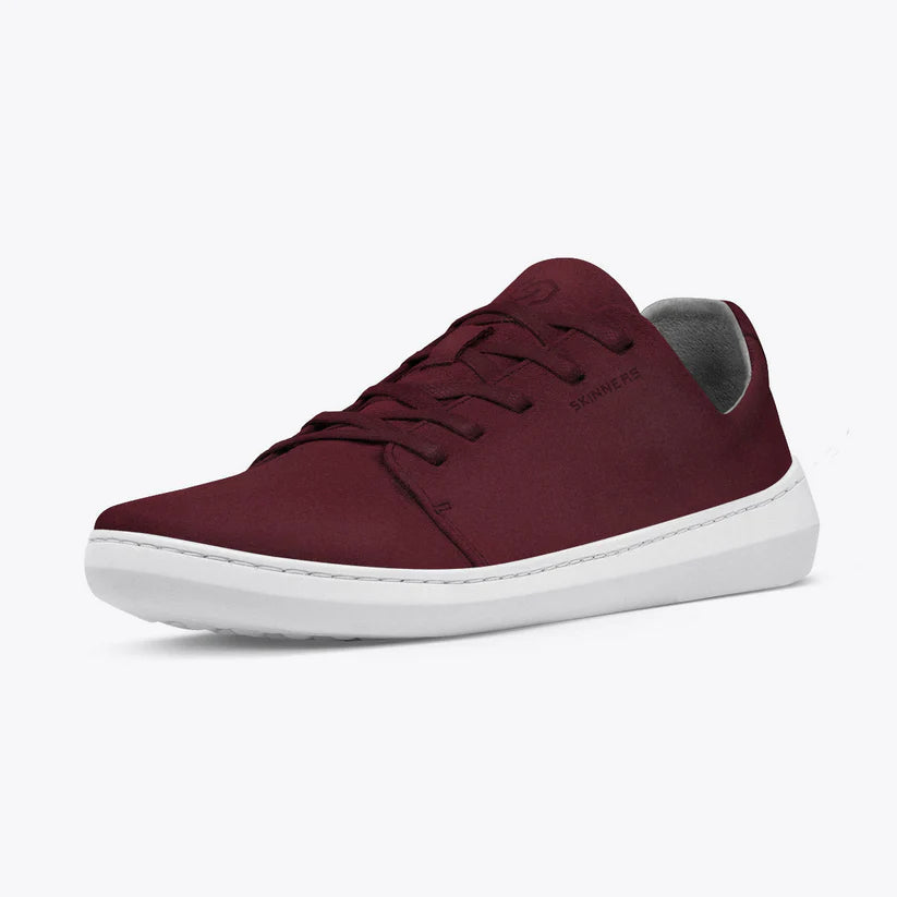 The Skinners Easygoer (Unisex) is a burgundy split leather low-top sneaker with a white sole, matching laces, and a subtle side logo. Handmade in Portugal, it's shown against a plain light background.