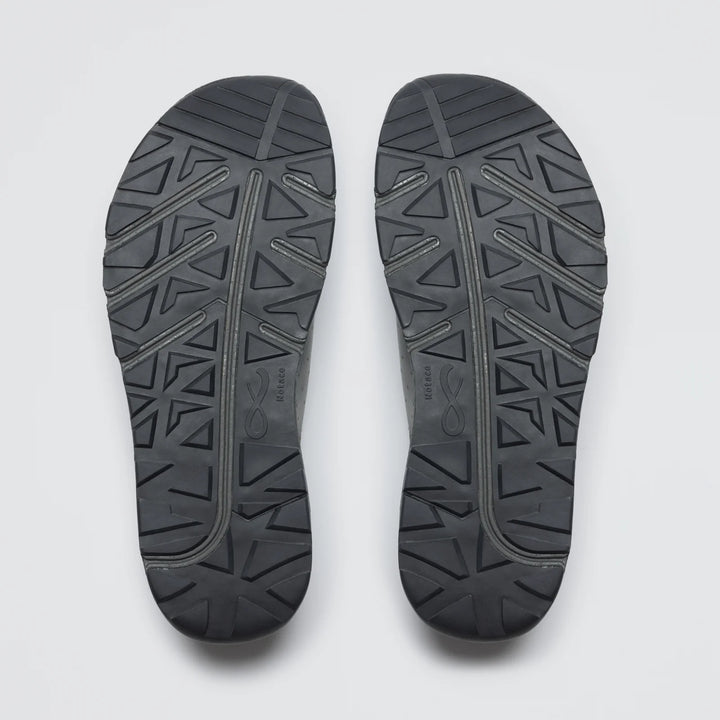 A pair of Notace Yama T1 men's trail shoe soles in black, featuring a geometric tread with triangles and diagonal lines, designed for all-day comfort, are displayed side by side on a plain white background.