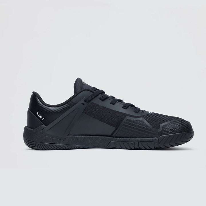 The Notace Koto 1 (Women's) is a black court shoe with a low profile, textured sole, and geometric design accents for grounded stability, displayed in side view against a plain light background.