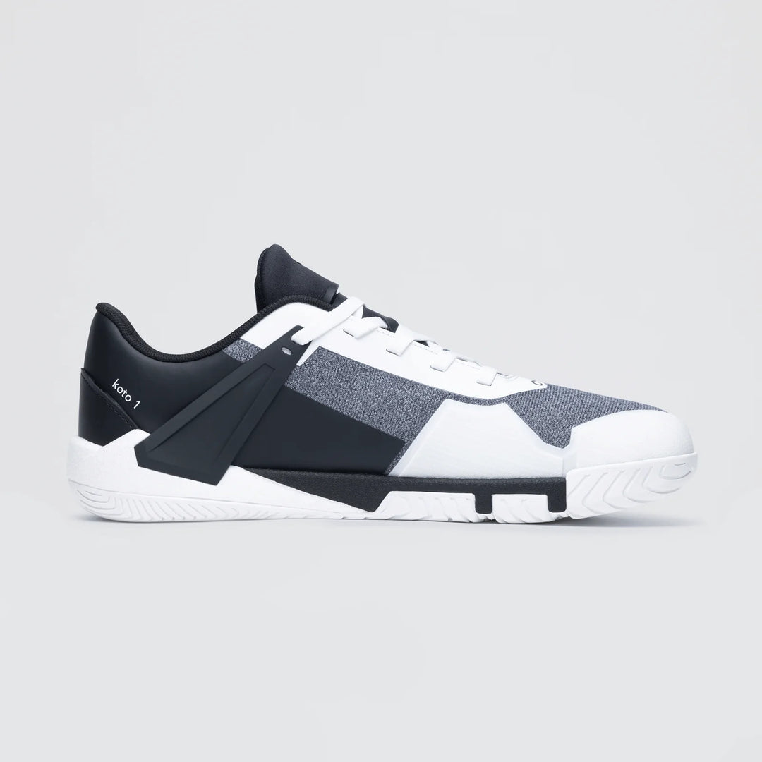 The Notace KOTO 1 (Men's) is a stylish low-top gym shoe in black, white, and gray with a modern geometric design and textured sole for multidirectional control, shown on a light gray background.