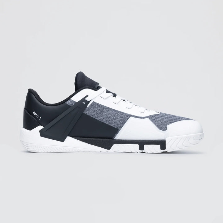 The Notace KOTO 1 (Men's) is a stylish low-top gym shoe in black, white, and gray with a modern geometric design and textured sole for multidirectional control, shown on a light gray background.