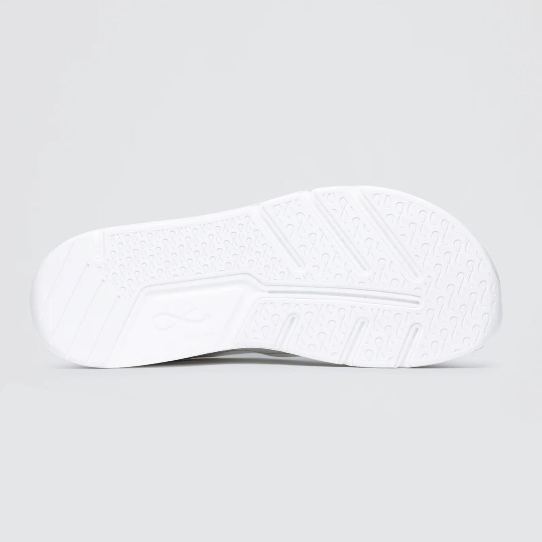 The image shows the white sole of the Notace Michi 1 (Women's) training shoe, with a flexible build and a textured pattern of diagonal lines, small circular indents, and grip zones for traction. The background is plain light gray.