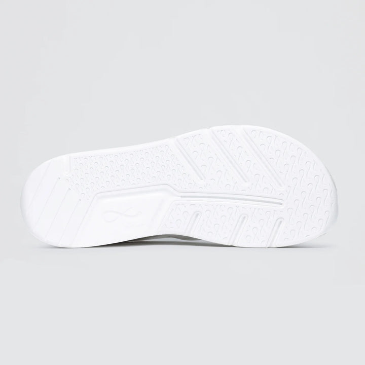 The image shows the white sole of the Notace Michi 1 (Women's) training shoe, with a flexible build and a textured pattern of diagonal lines, small circular indents, and grip zones for traction. The background is plain light gray.