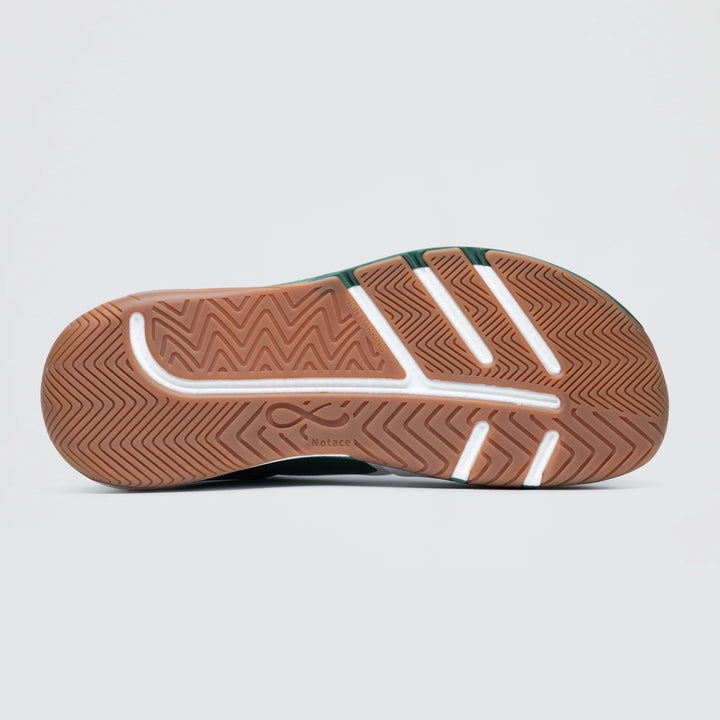 The image shows the sole of the Notace Koto 1 (Women's) court shoe with a brown herringbone-patterned tread for grounded stability, white lines and a logo in the center, and green details visible on the upper edge.