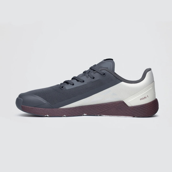 The Notace Michi 1 (Men’s) is displayed in profile on a light background, highlighting its dark grey flexible upper with a white side panel, black laces, and a maroon sole featuring an eTPU midsole.