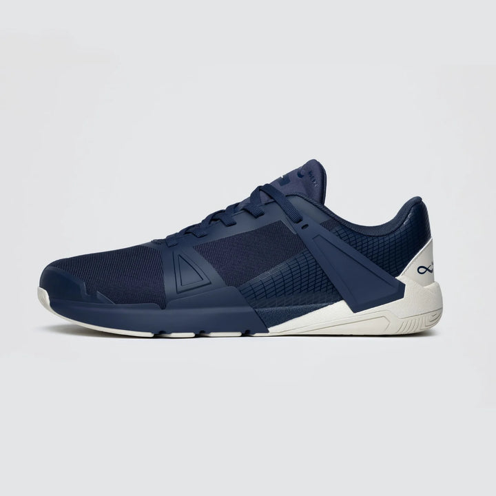 The Notace Koto 1 (Women’s) is displayed in side profile against a plain light gray background, featuring a navy blue mesh upper with geometric design accents and a white sole—engineered for multidirectional control.
