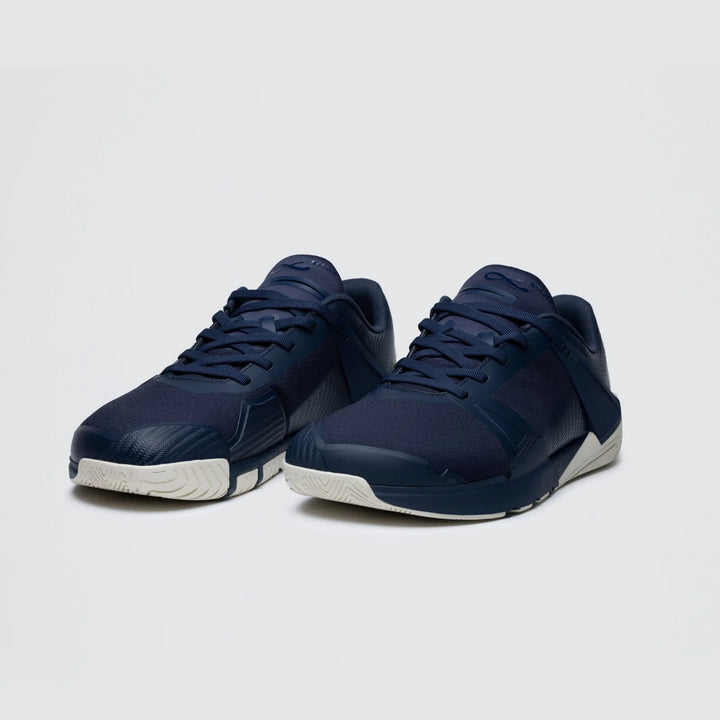 A pair of Notace Koto 1 (Women’s) dark blue athletic sneakers, engineered for multidirectional control and featuring white soles, are positioned on a light gray background, angled slightly to the left.