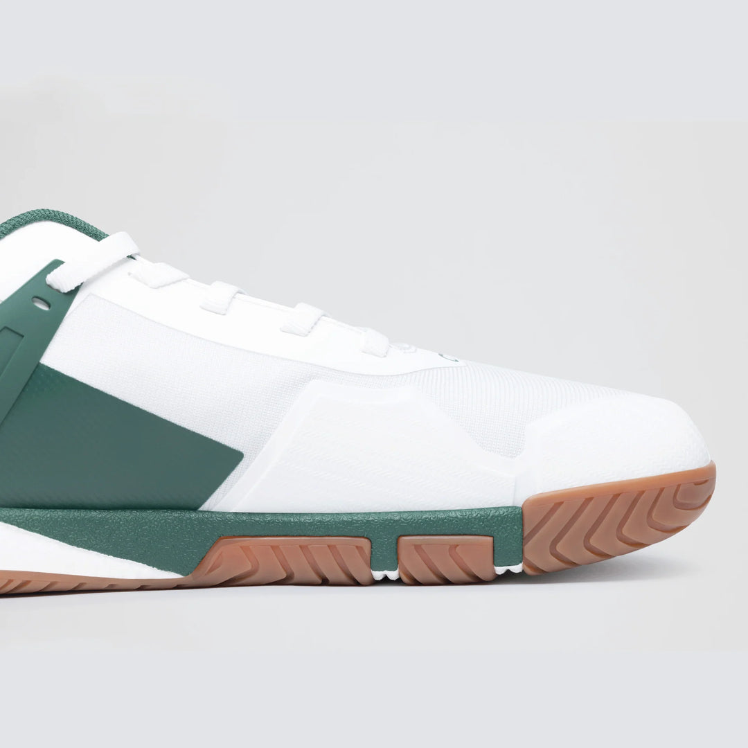 A close-up side view of the Notace Koto 1 (Women's) court shoe in white with green accents and a gum-textured sole, designed for stability, shown against a light gray background.