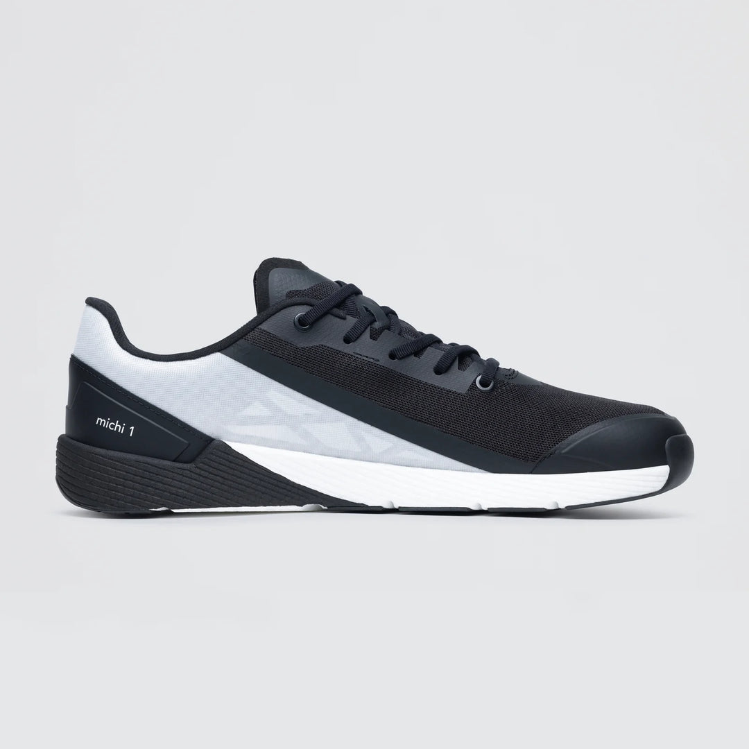 The Notace Michi 1 (Women's) is a black and gray low-profile athletic sneaker with white accents, black laces, mesh upper, textured sole, and “michi 1” on the heel—perfect as a lightweight road to gym shoe.