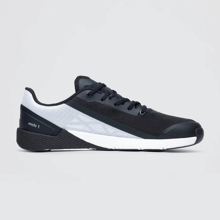 The Notace Michi 1 (Women's) is a black and gray low-profile athletic sneaker with white accents, black laces, mesh upper, textured sole, and “michi 1” on the heel—perfect as a lightweight road to gym shoe.