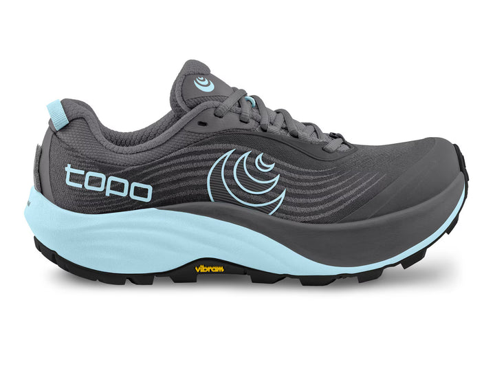 The TOPO Pursuit 3 (Women’s) is a gray trail running shoe featuring light blue accents on the sole, logo, and heel tab. TOPO branding appears on the side, while the Vibram Megagrip technology is showcased on the blue and black outsole. This zero-drop trail runner provides a cushioned platform for comfortable off-road adventures.