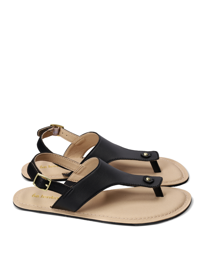 A pair of BeLenka Promenade 2.0 (Women's) minimalist sandals in black and tan, featuring an elegant thong strap, ankle buckle, and gold-tone rivet details, displayed on a white background.