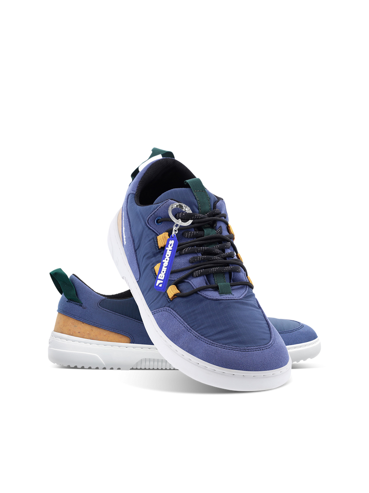 The Barebarics Revive (Men's) is a pair of blue casual sneakers with white soles, dark blue laces, green and tan accents, made from vegan materials for barefoot comfort and lightness, featuring a detachable blue DARKWOOD tag on a plain white background.