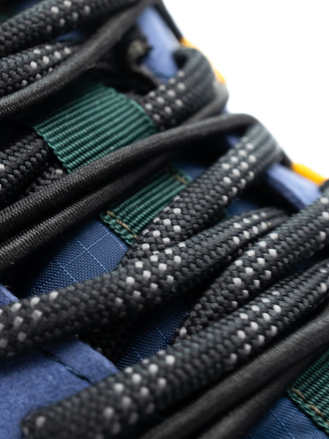 Close-up of black shoelaces with white speckles through green and blue eyelets on the navy blue Revive (Men's) by Barebarics, a lightweight shoe made from vegan materials.