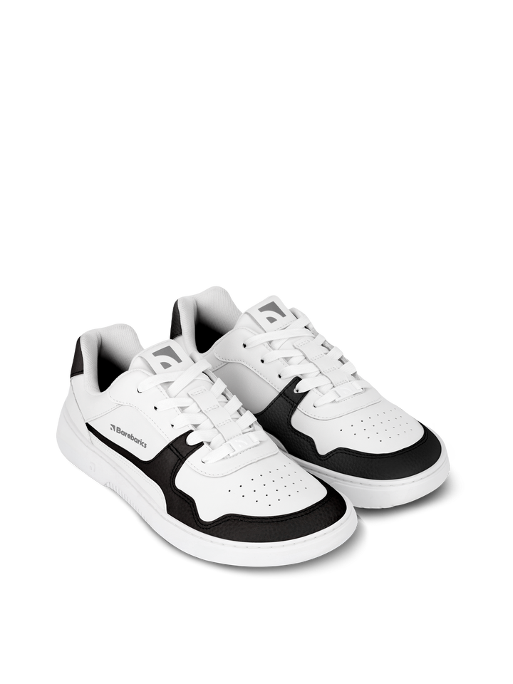 The Barebarics Zing (Unisex) sneakers feature a white design with black accents on the sides, toe, and heel, made from sustainable leather. These low-cut shoes offer barefoot-quality comfort and are shown against a plain white background.