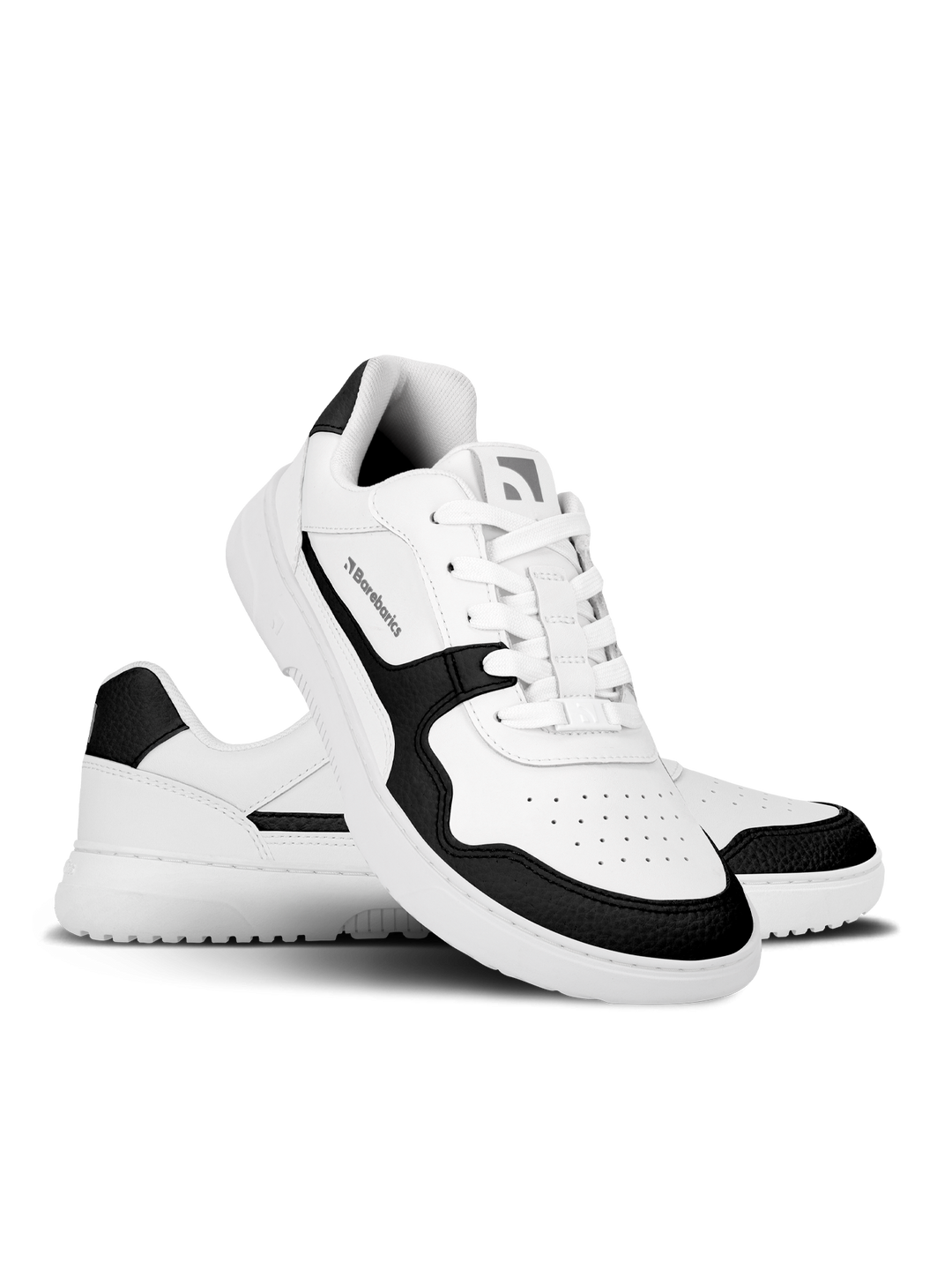 The Barebarics Zing (Unisex) sneakers feature a white design with black accents on the toe, heel, and sides. One shoe stands upright as the other is tilted to showcase its sole and perforated sustainable leather detailing.