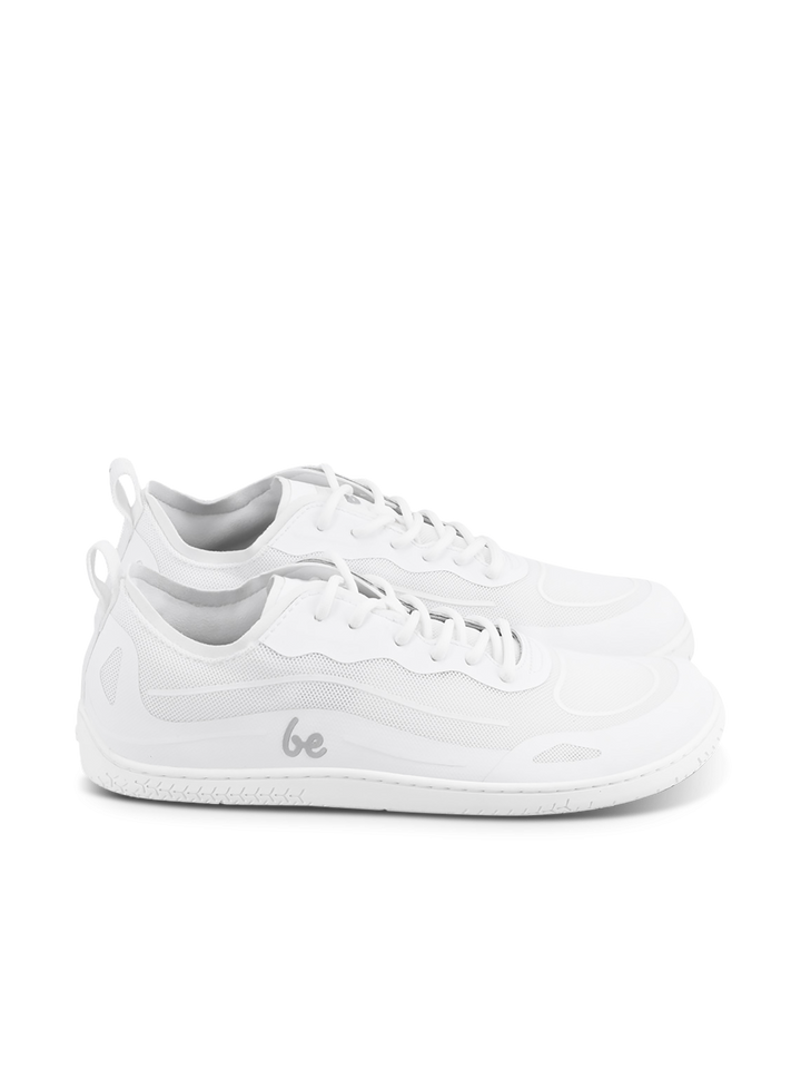 A pair of BeLenka Velocity unisex white low-top sneakers featuring mesh and synthetic material details, white laces, a flexible sole, and the word "be" printed in gray on the side.