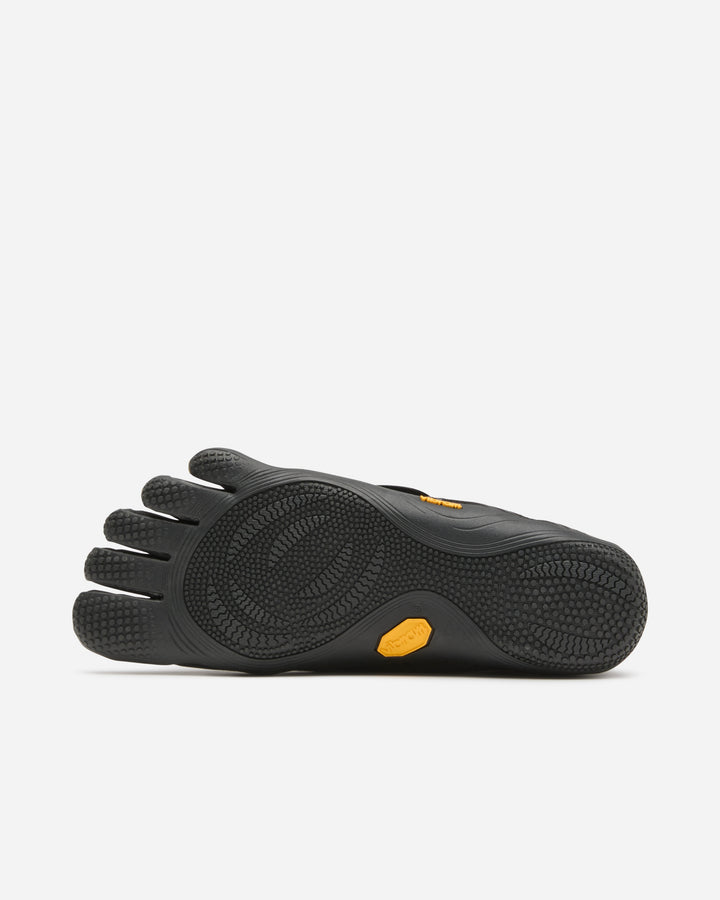 The Vibram Groundsplay (Women's) is a black minimalist shoe with individual toe sections, a textured rubber sole for grip, and yellow logo accents—ideal for weightlifting or circuit training.