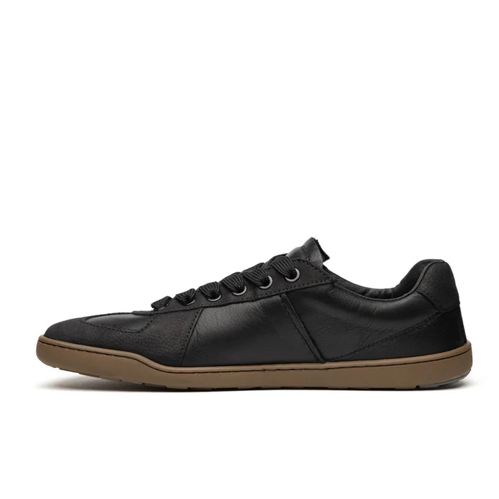 Introducing the BluSun BLSN-200 (Men’s): a black low-top sneaker with black laces and a brown rubber sole, displayed in profile against a white background. This barefoot shoe is thoughtfully crafted with an organic cotton lining for enhanced comfort.