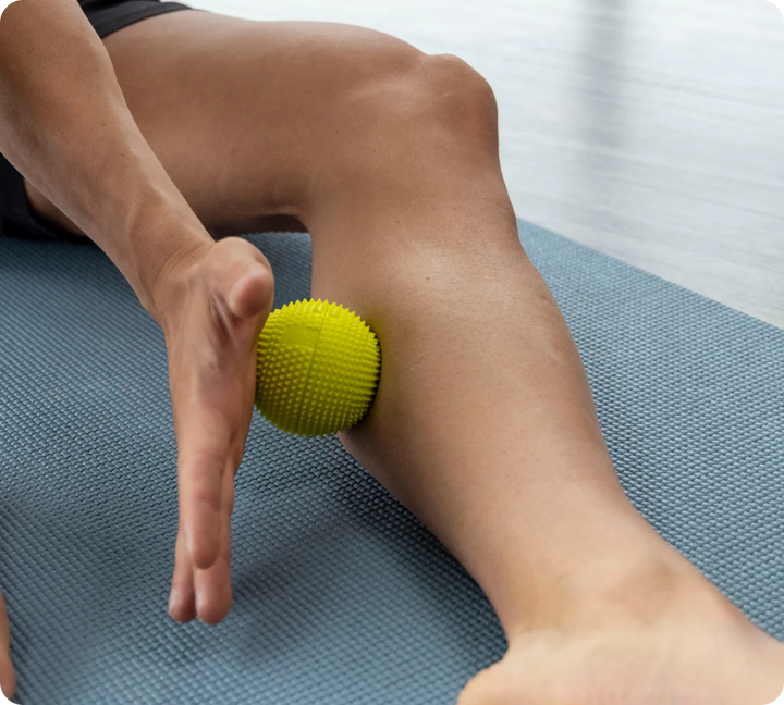 A person uses the NABOSO Neuro Ball to massage their lower leg while lying on a blue exercise mat.