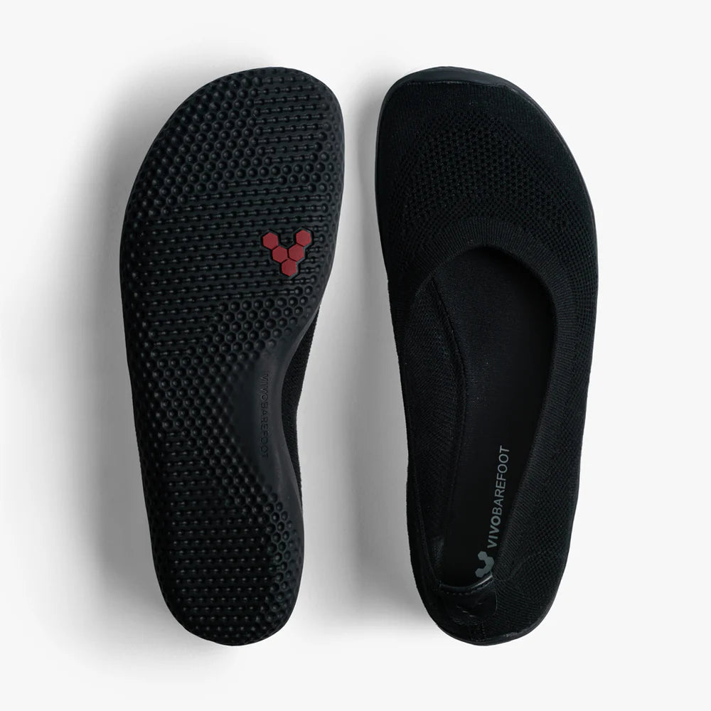 The VIVOBAREFOOT Asana Yin Ballerina Knit (Women's) are black slip-on shoes with textured soles, a subtle red logo underneath, and minimalist rounded-toe design. The interior displays VIVOBAREFOOT branding. Shown on a white background.
