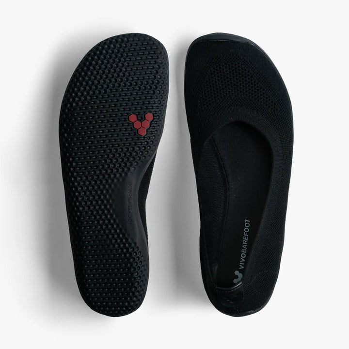 The VIVOBAREFOOT Asana Yin Ballerina Knit (Women's) are black slip-on shoes with textured soles, a subtle red logo underneath, and minimalist rounded-toe design. The interior displays VIVOBAREFOOT branding. Shown on a white background.